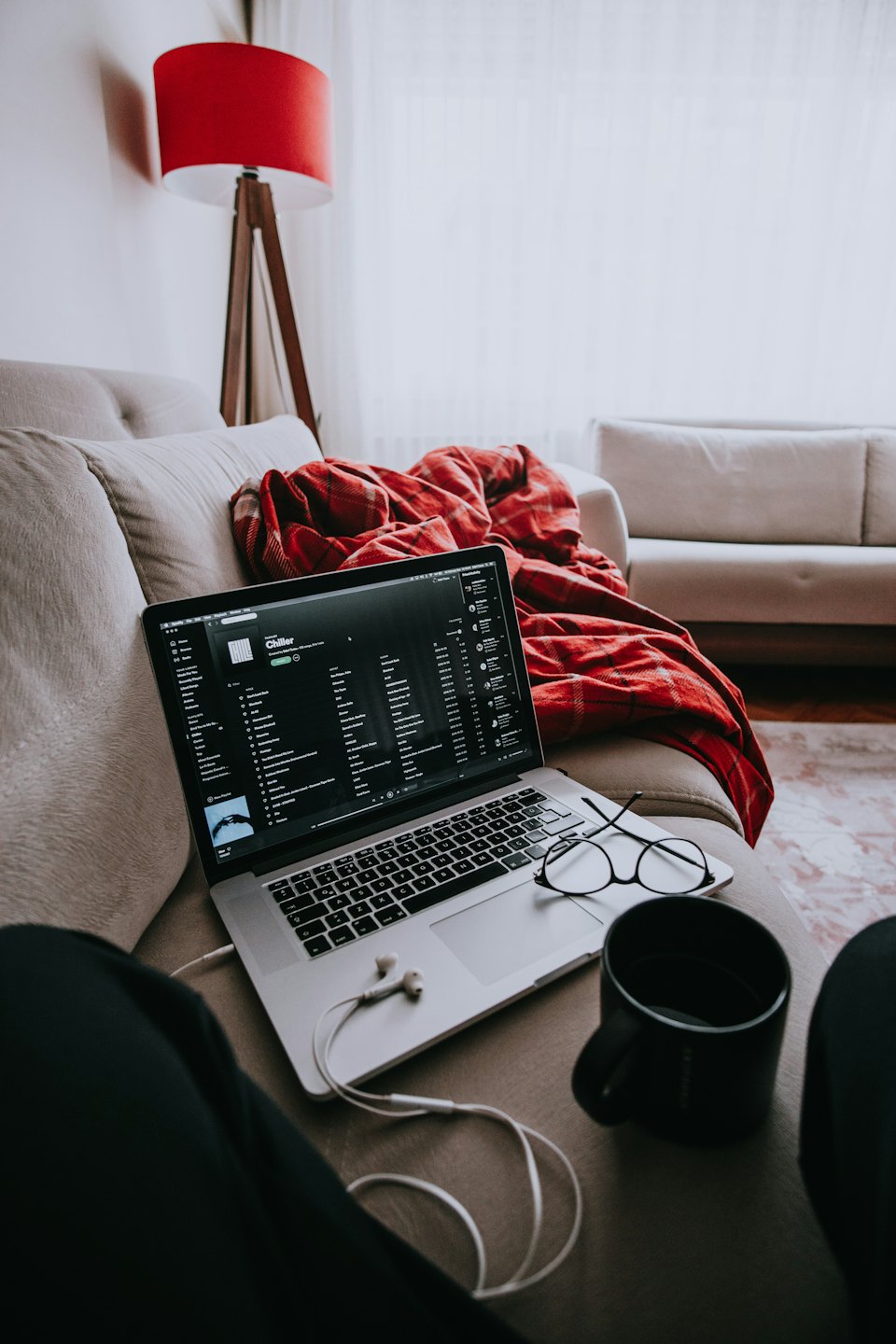 Offener Laptop mit Musikdienst auf dem Sofa, daneben Kopfhörer und eine Decke.